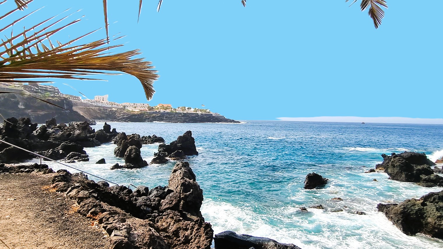 Sunny bay in Tenerife with black rocks and blue sea.